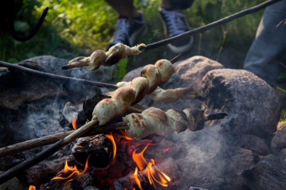 ruoka-kettukallion-elmystila-stick-buns-over-campfire_35607007555_o_590x people barbecuing over fire